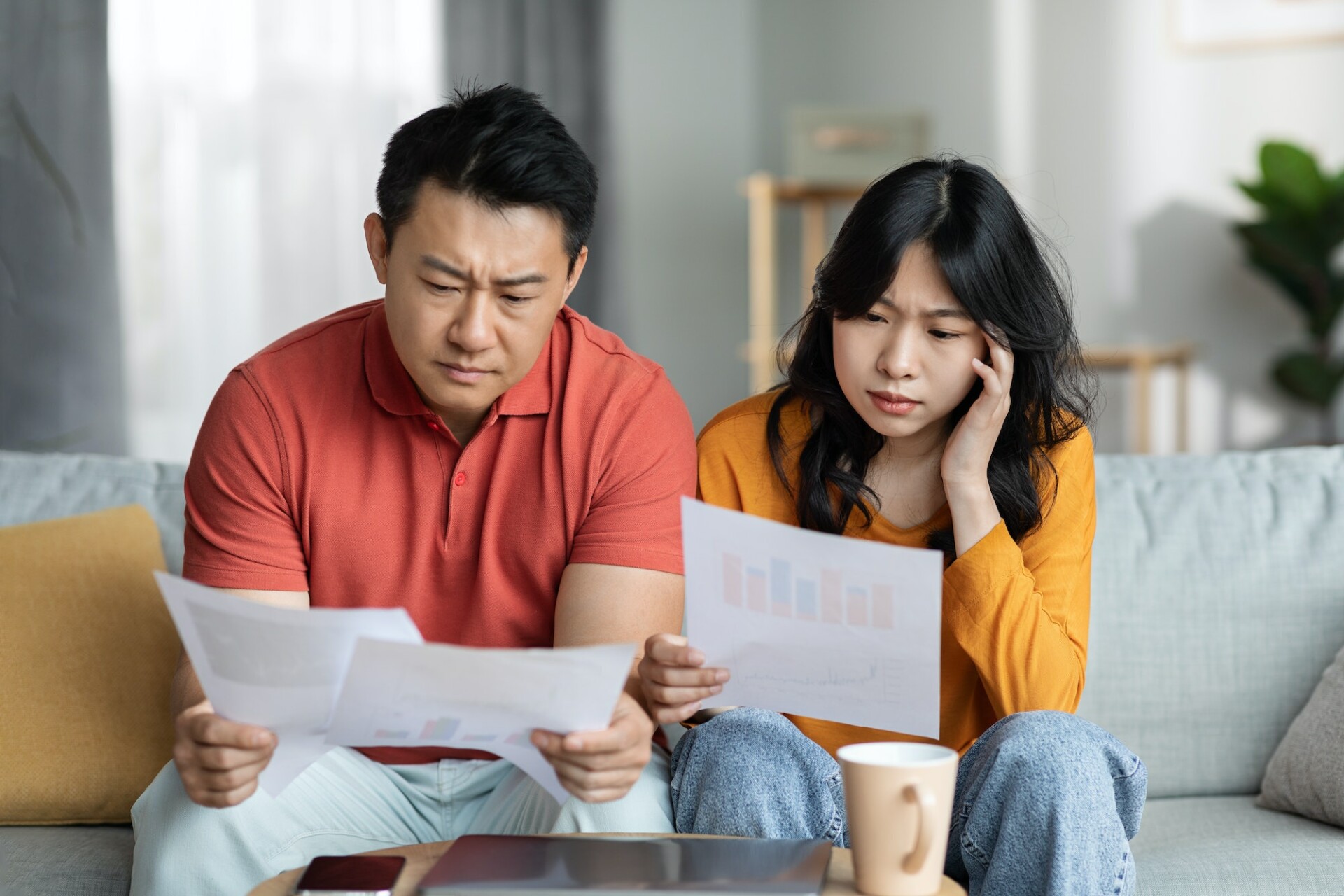 Confused asian couple checking bills, home interior