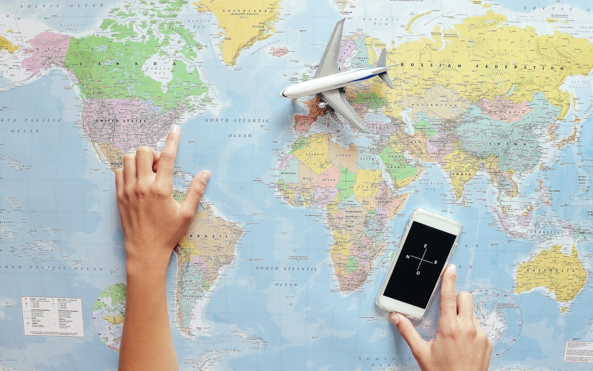 Top view of young tourist woman pointing her next travel destination using world map and phone